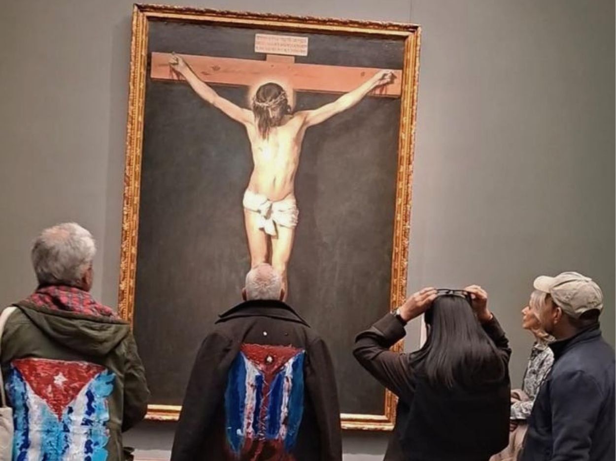 Performance "Mi bandera" del artista cubano exiliado Rafael Vilches, junto al artivista Rigoberto Carceller. Frente al cuadro "Cristo crucificado" (1632) de Diego Velázquez en el Museo del Prado (23 de marzo de 2026). Foto de Ana Rosa Díaz Naranjo.