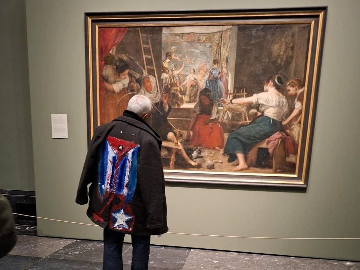 El artiPerformance "Mi bandera" del artista cubano exiliado Rafael Vilches. El artivista cubano Rigoberto Carceller frente al cuadro "La fábula de Aracné" (1657) de Diego Velázquez en el Museo del Prado (23 de marzo de 2026). Foto de Ana Rosa Díaz Naranjo.