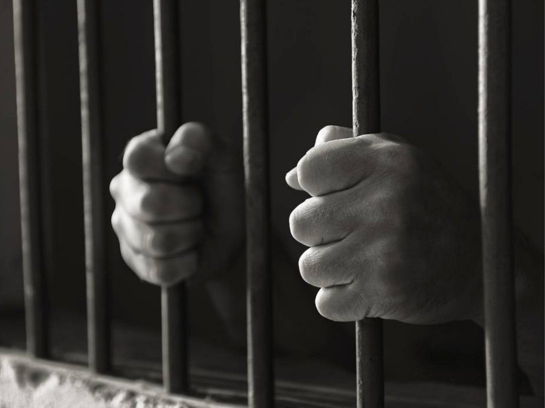 Manos de preso y barrotes cárcel