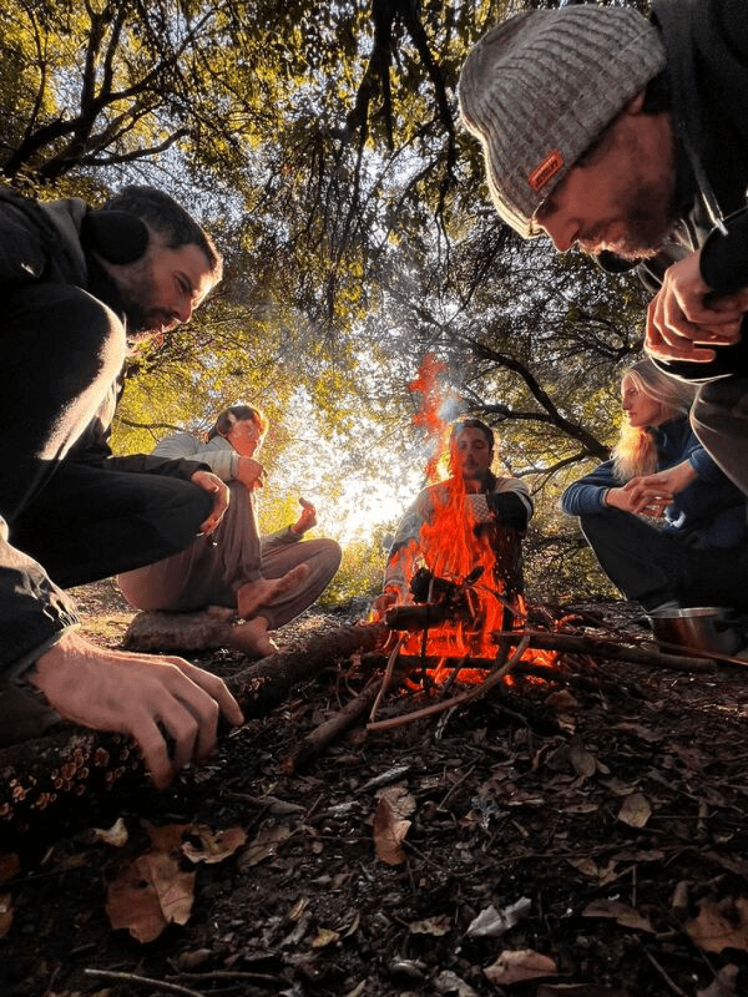 Grupo de personas sentadas alrededor de la una fogata en el bosque.