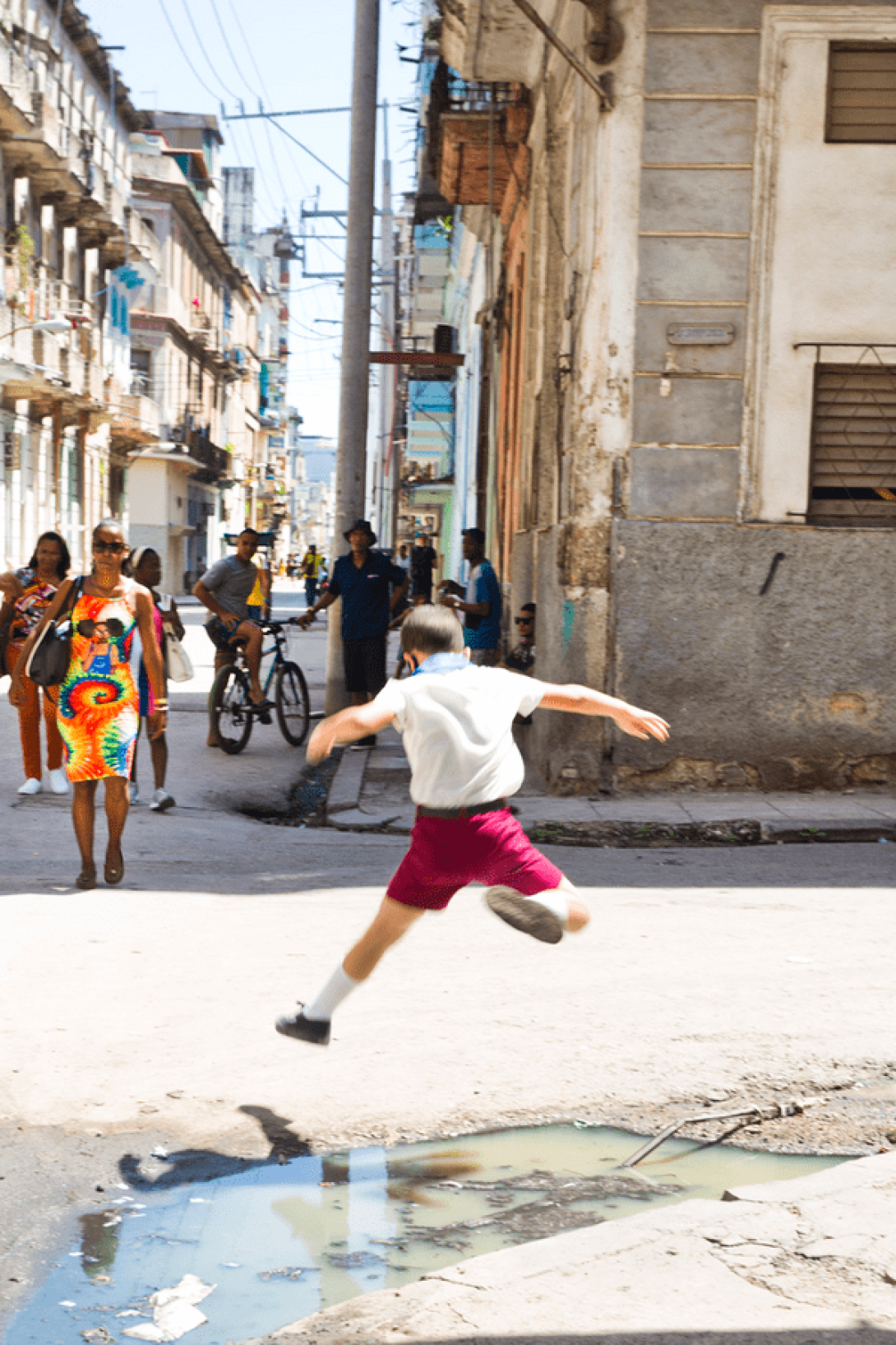 Niño salta sobre un charco de agua en la calle. 