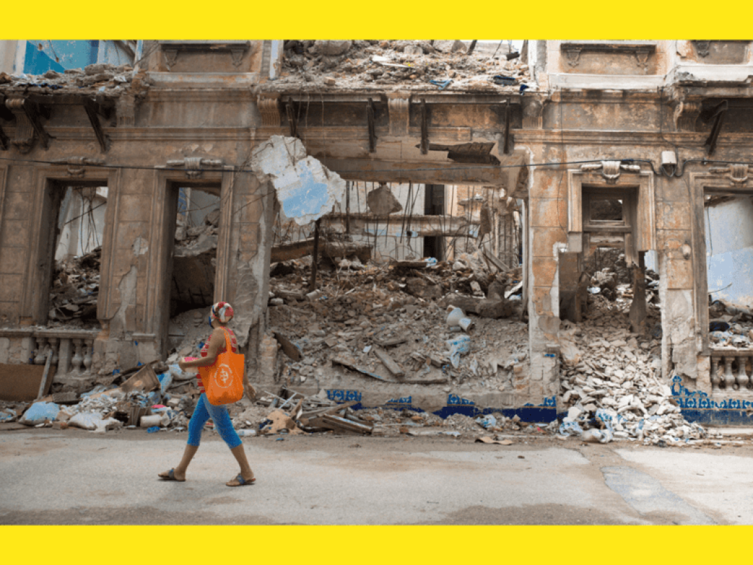 Mujer pasa frente a un edificio derrumbado.