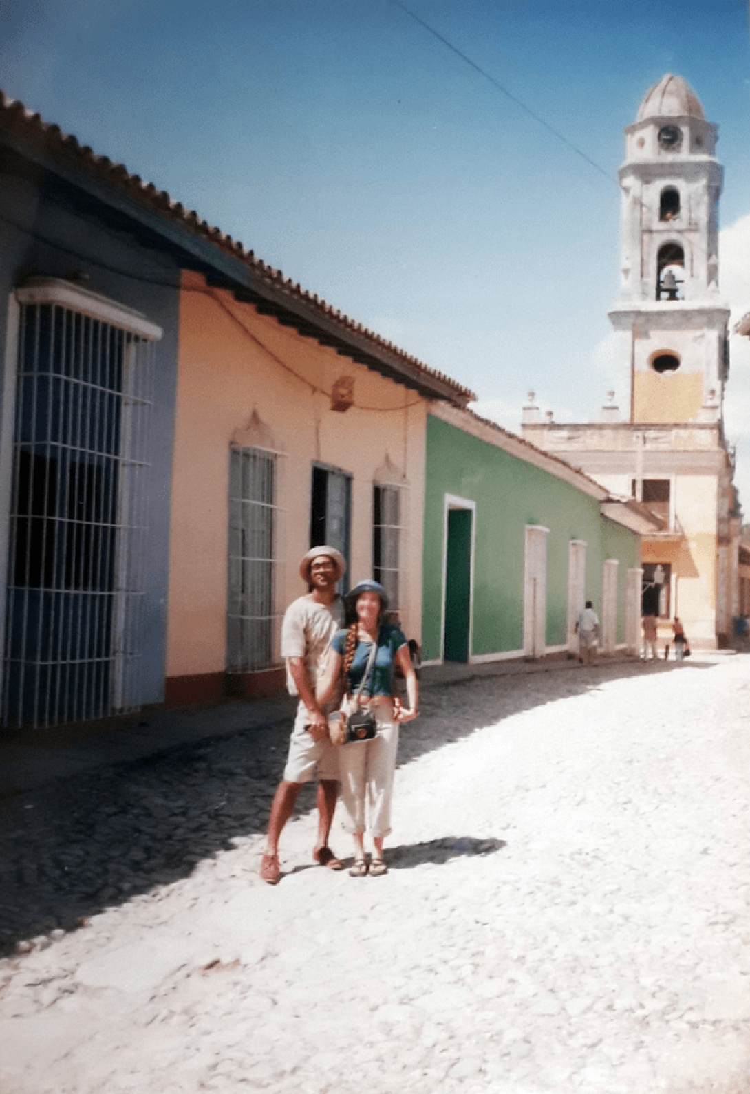 Dos personas posando en una calle de Trinidad. Al fondo, su torre insignia.