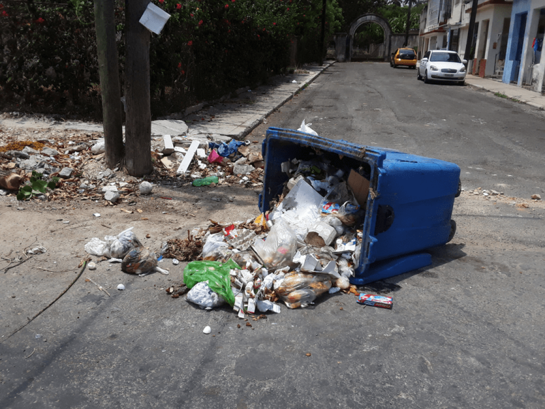 Contenedor de basura volcado en la calle vertiendo la basura alrededor.