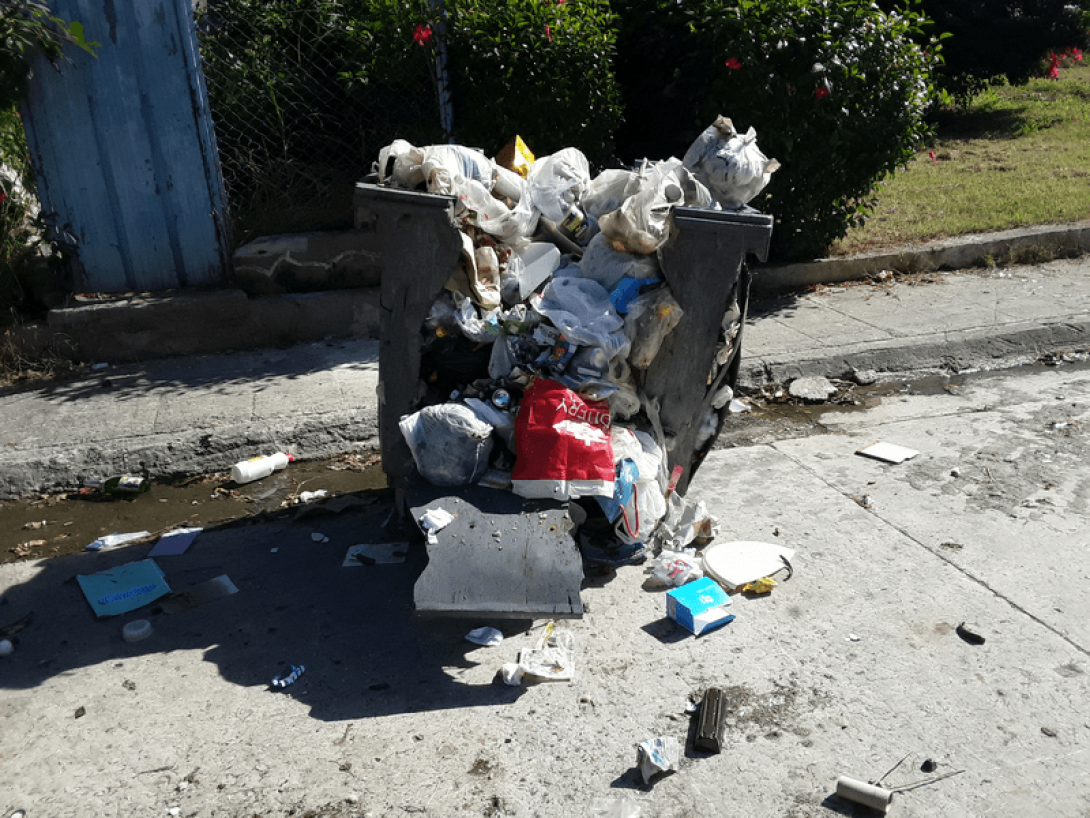 Contenedor de basura roto y desbordado de desperdicios.