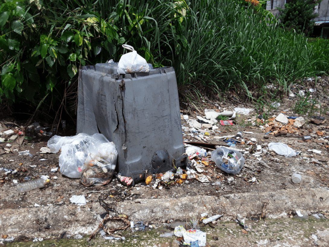 Contenedor de basura volcado en la calle vertiendo la basura alrededor.