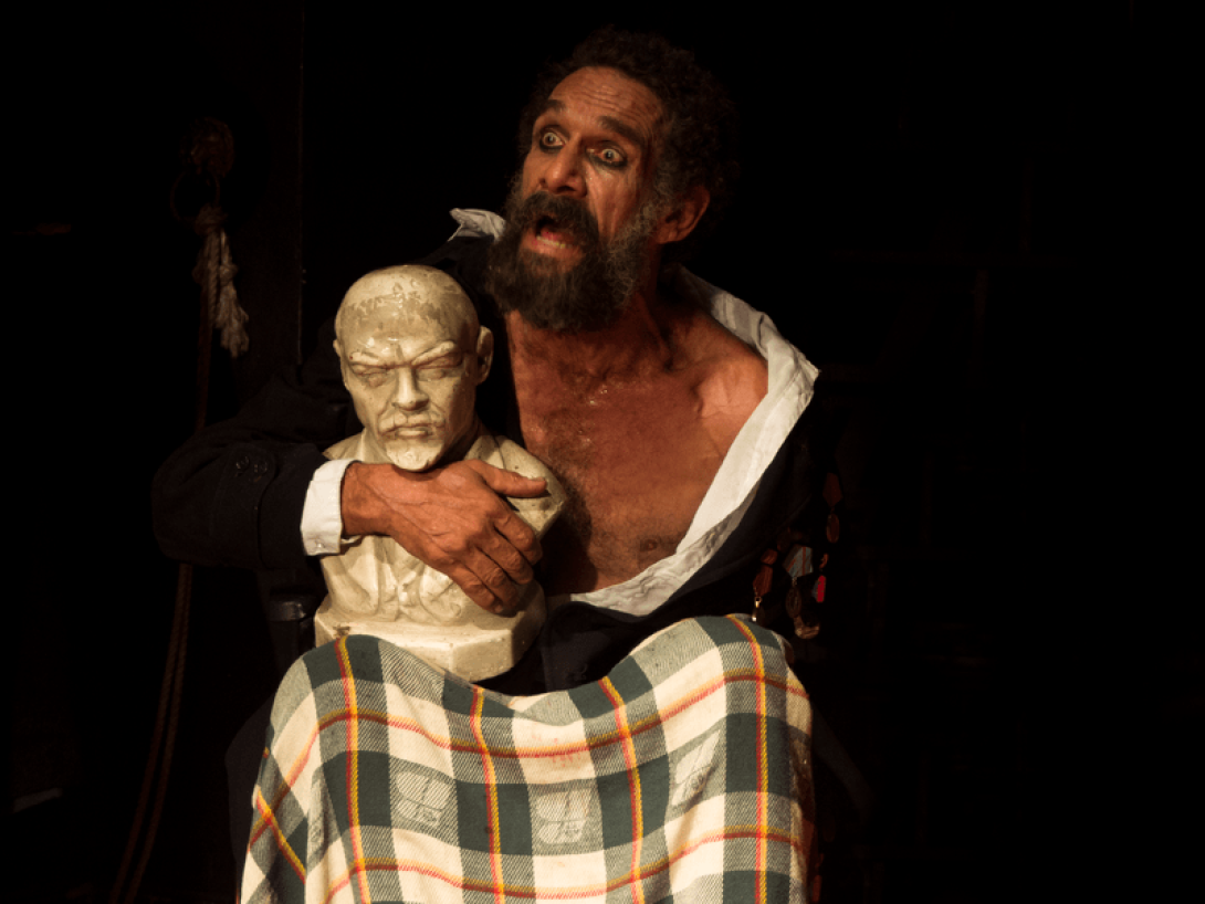 Actor en escena sostiene un busto de Lenin.