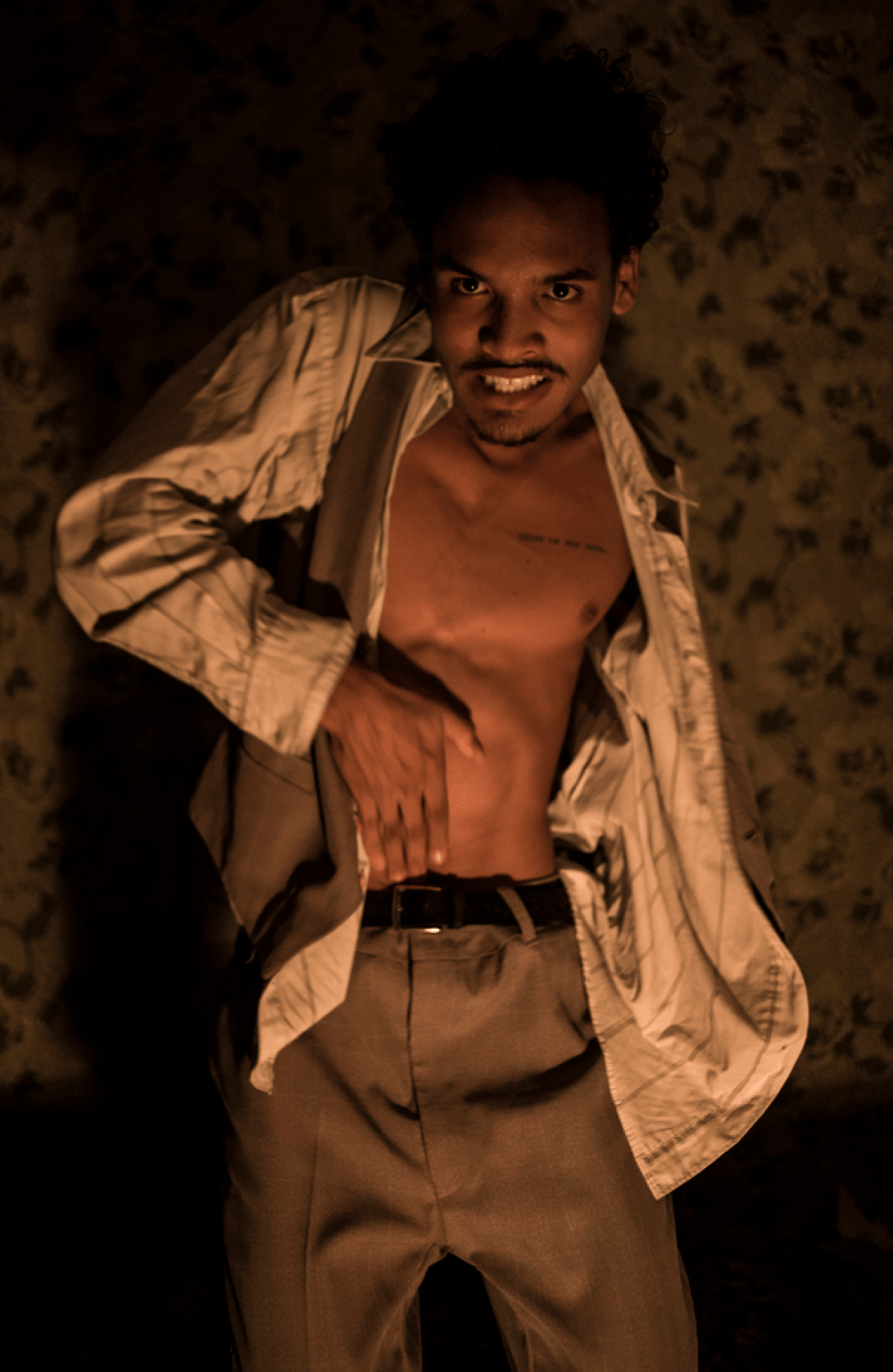 Actor con la camisa abierta y el torso descubierto toca su vientre con la mano.