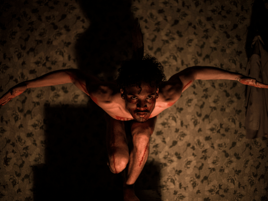 Actor semidesnudo abre su brazos y mira hacia arriba.