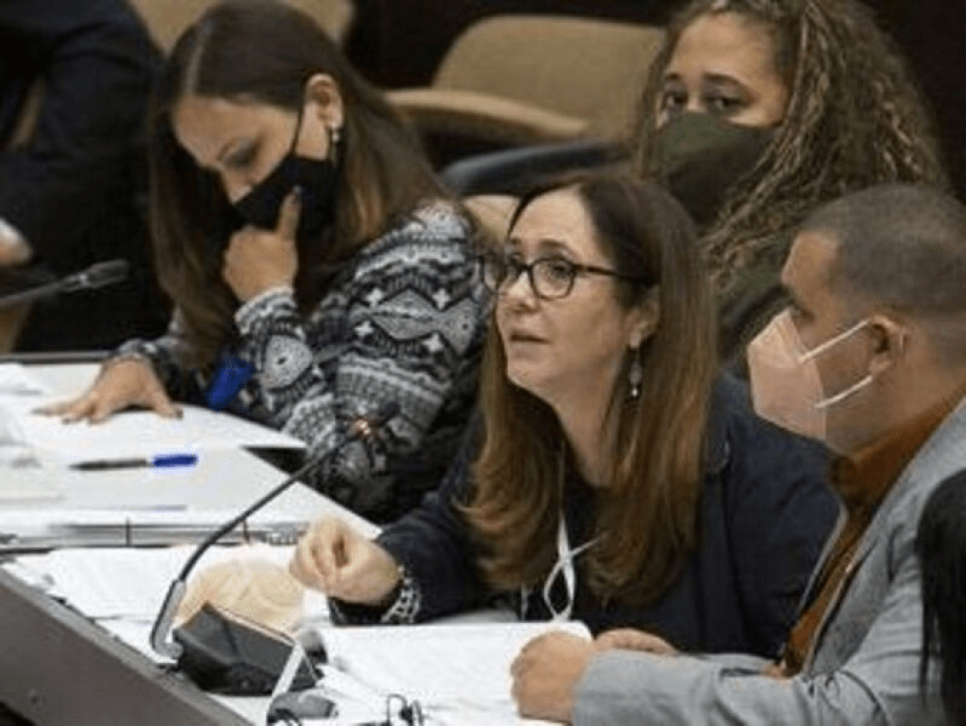 Mujer hablando rodeada de otras personas.