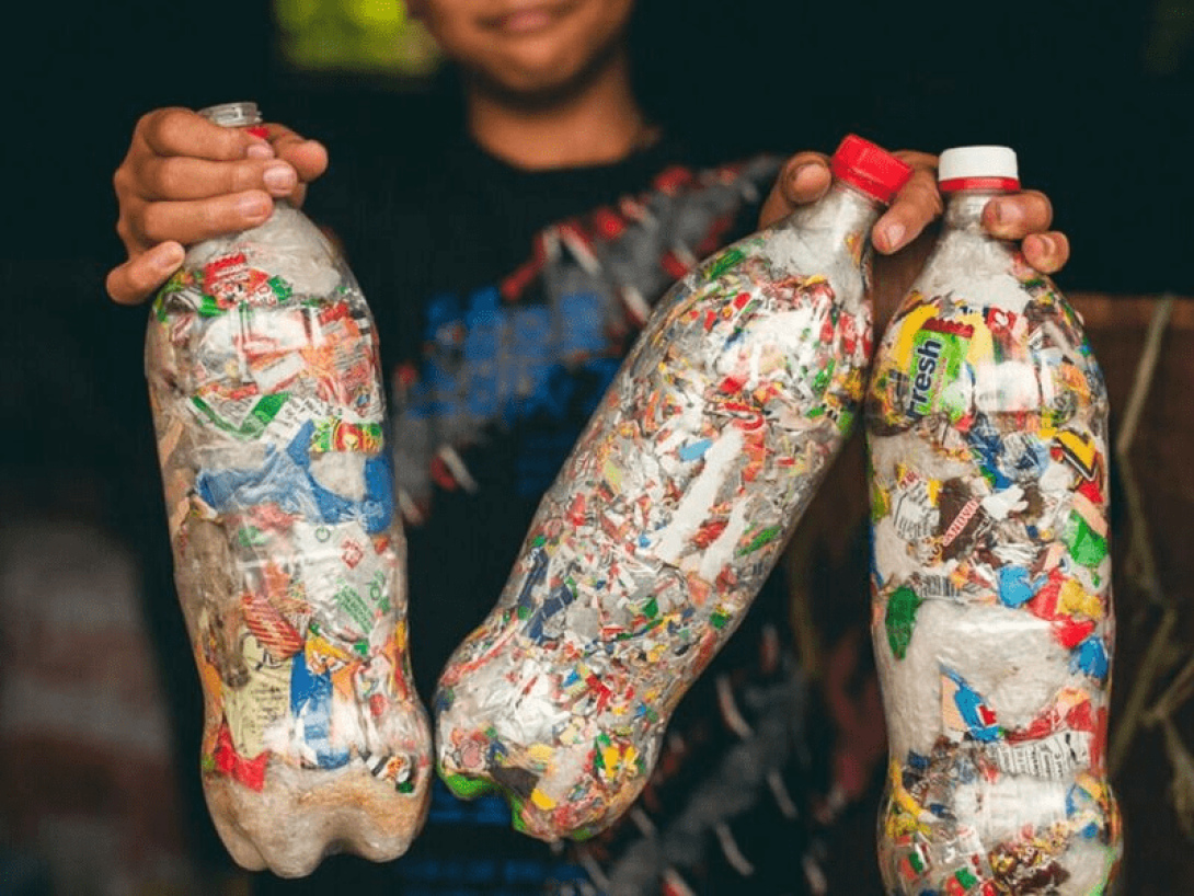Niño mostrando varias botellas plásticas convertidas en ecoladrillos.