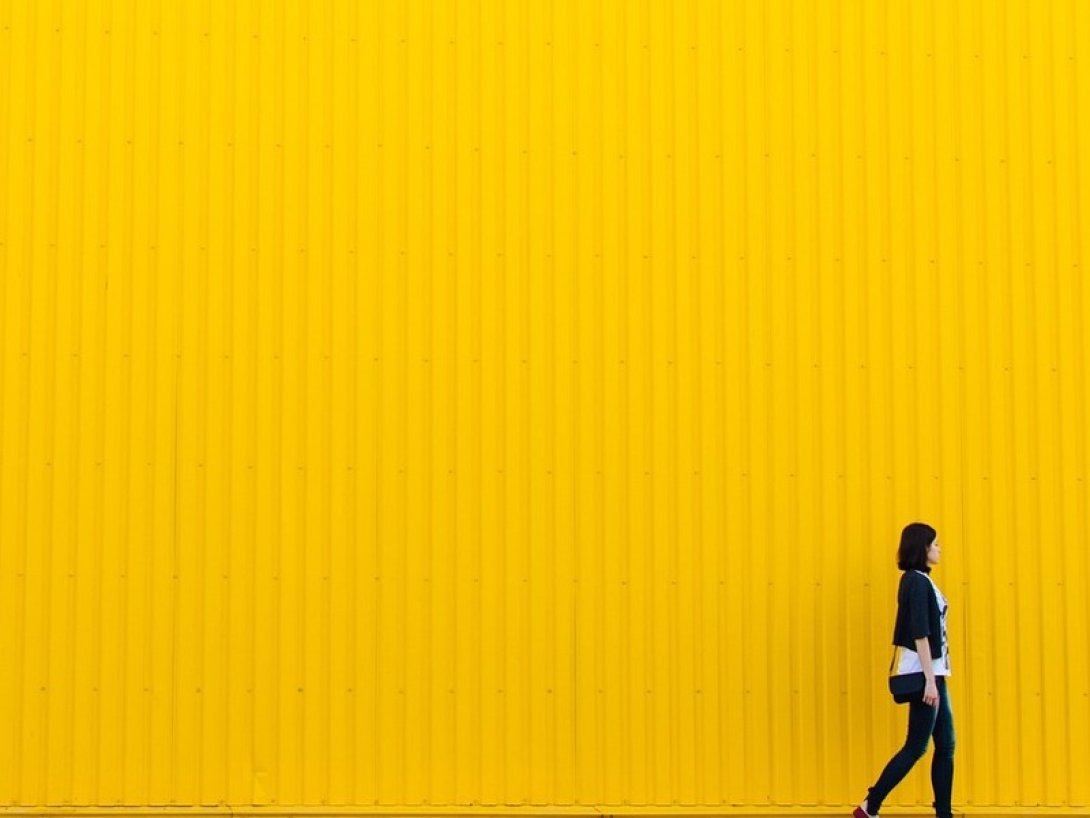 Mujer caminando, al fondo una pared amarilla.