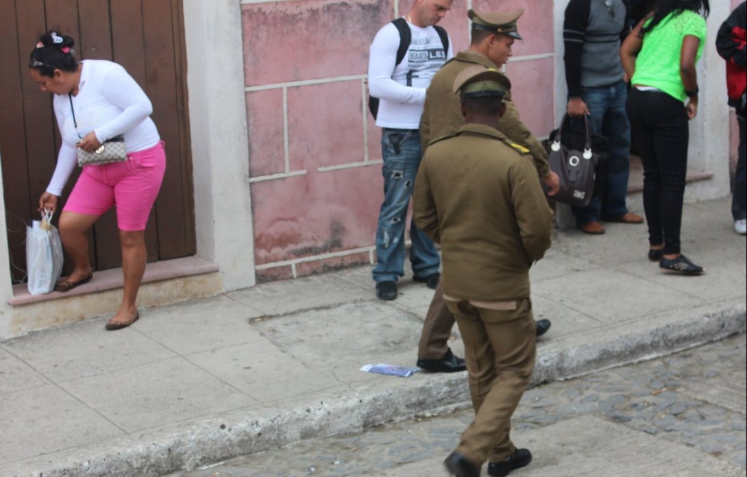 Ejemplar de la revista Árbol Invertido en una acera, mientras personas caminan alrededor, policías.