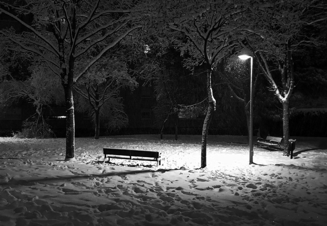 Banco de parque y farol encendido bajo la nieve.