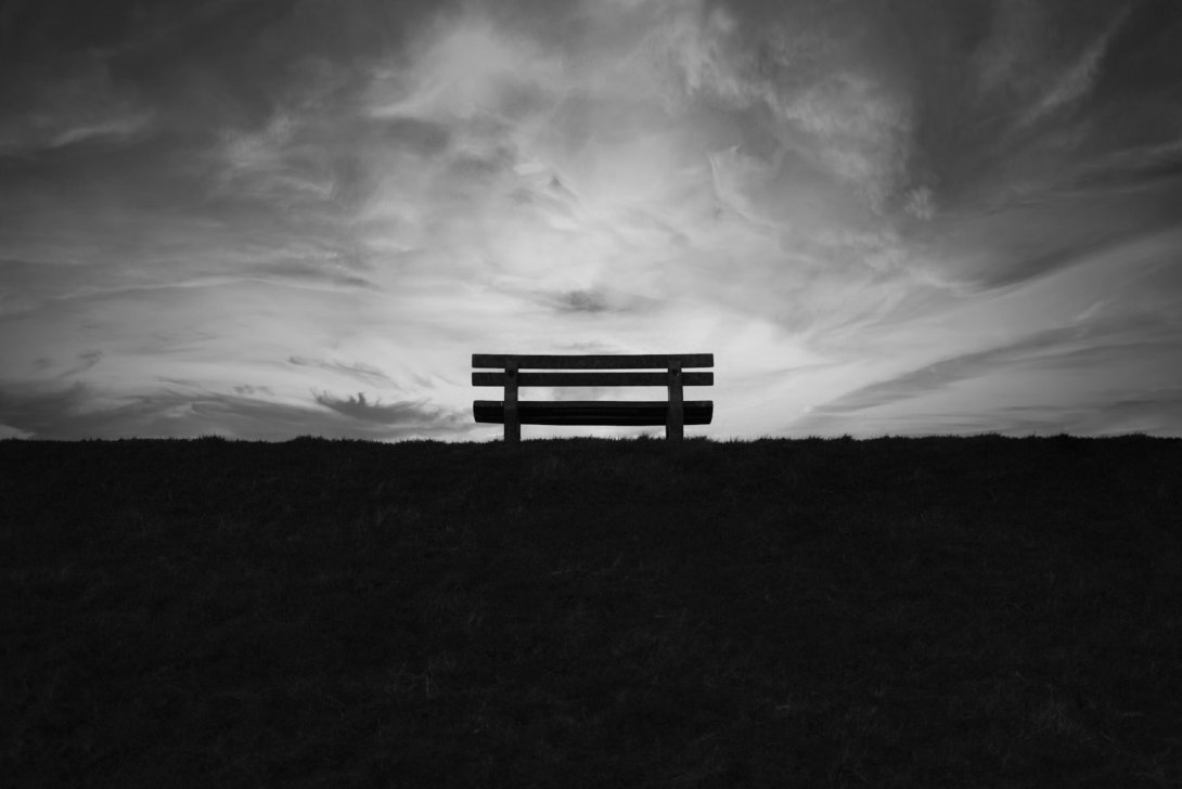Banco vacío en un paisaje al atardecer. Blanco y negro