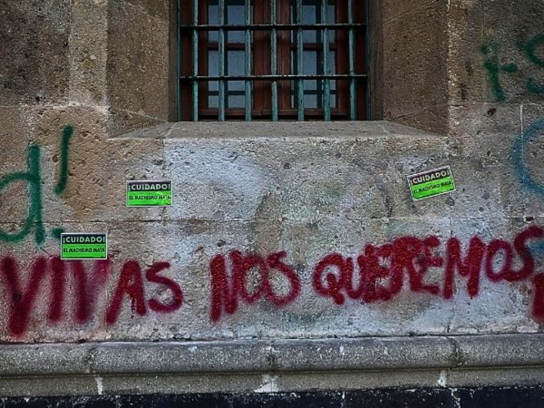 Grafiti en un muro con la frase “Vivas nos queremos” y carteles de advertencia sobre el feminicidio.