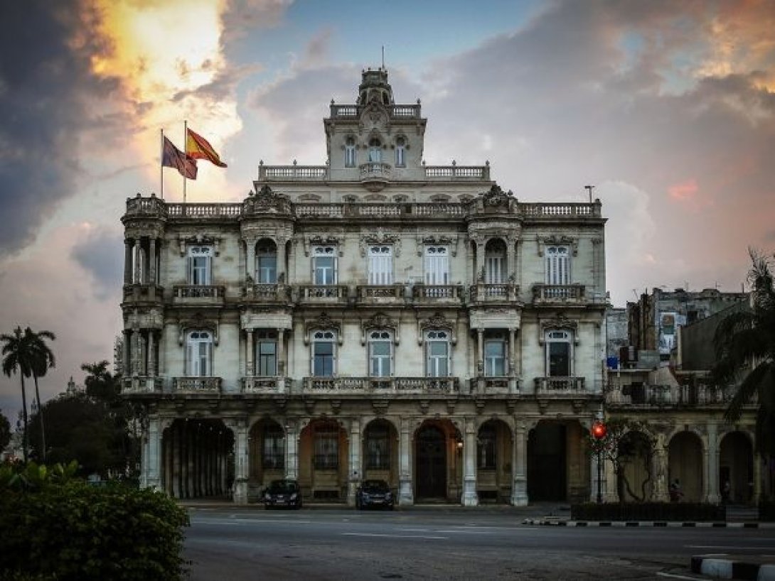 Fachada del Consulado de España en La Habana, edificio histórico con bandera española ondeando al atardecer.