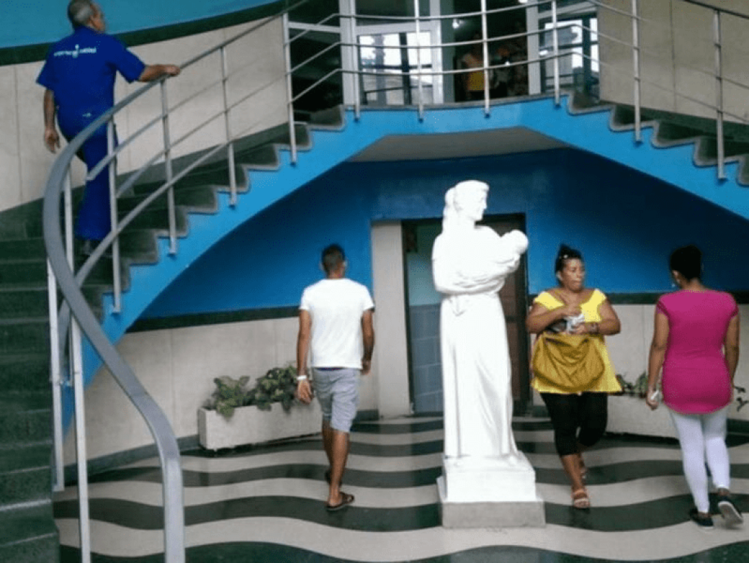 Persona transitando alrededor de la escultura a las madres en el salón del Hospital Hijas de Galicia, La Habana.