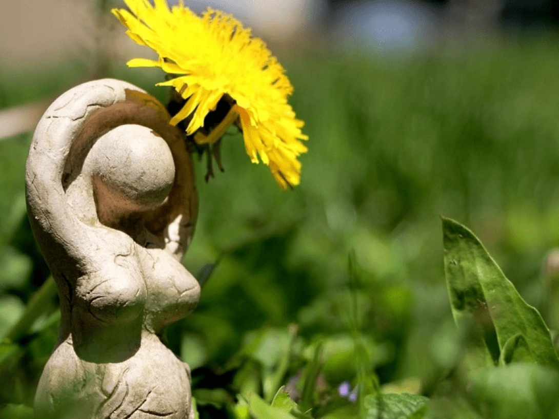 Figura de una diosa pagana con una flor en la yerba.