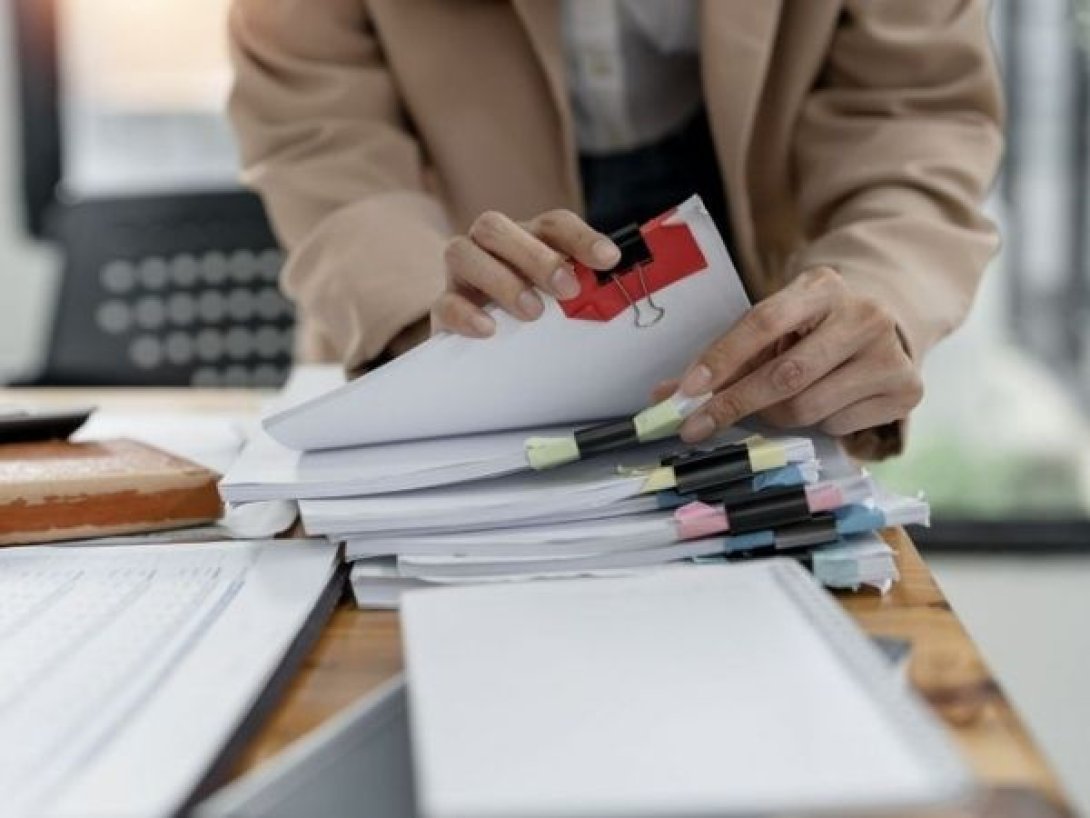 Persona organizando documentos y formularios con clips de colores sobre un escritorio.
