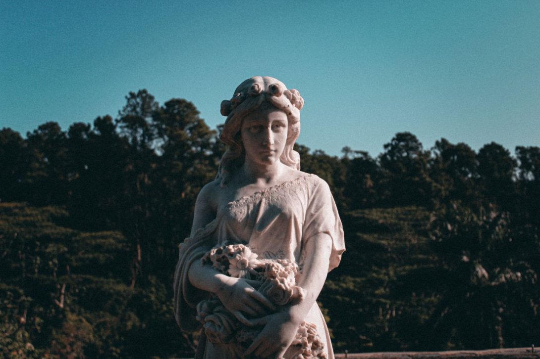 Estatua de mujer con flores en brazos.