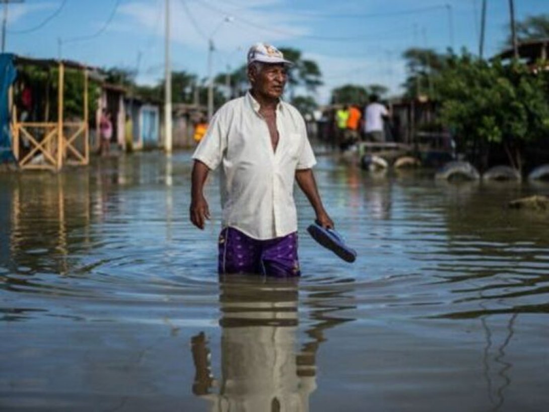 Persona camina por una calle con agua hasta la cintura a causa de una inundación.