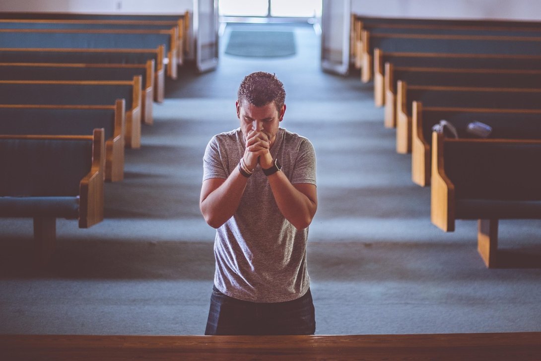 Hombre orando en un templo abierto y vacío. Iglesia con bancos.