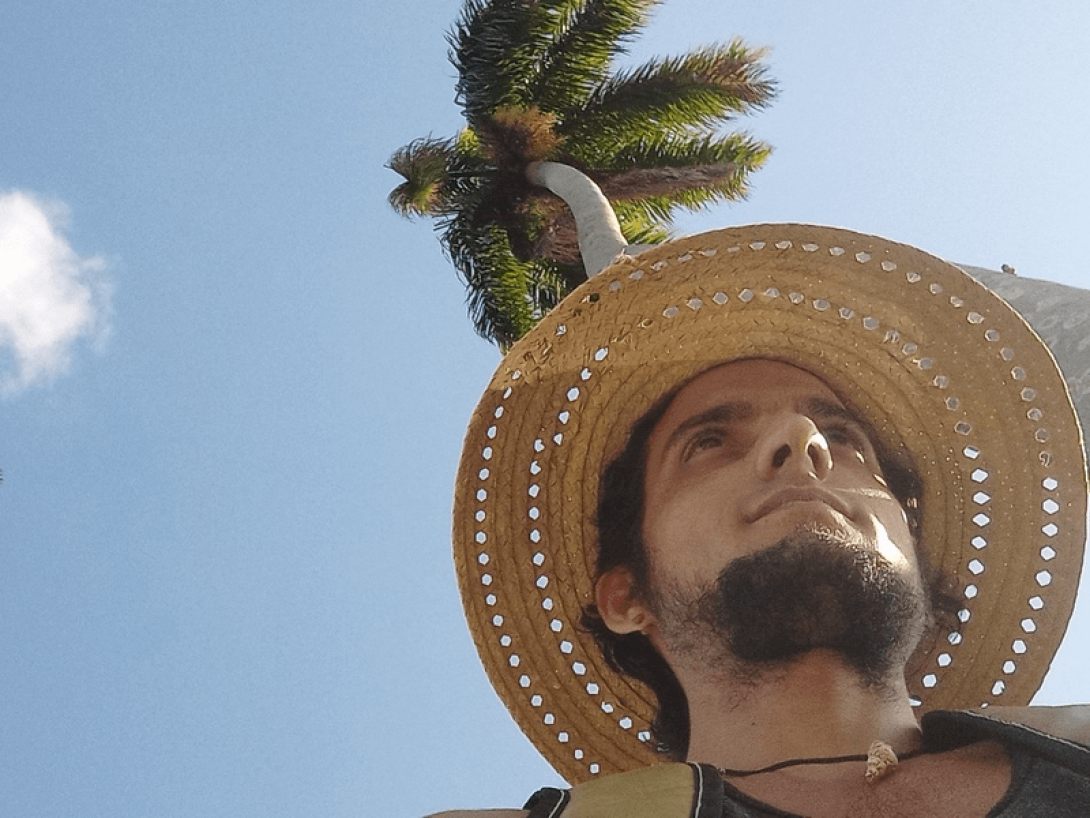 Rostro masculino con cielo azul detrás y una palma.