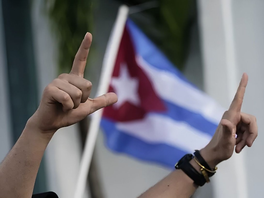 Un manifestante muestra la L de libertad con sus dedos frente a una bandera cubana. Foto: AP