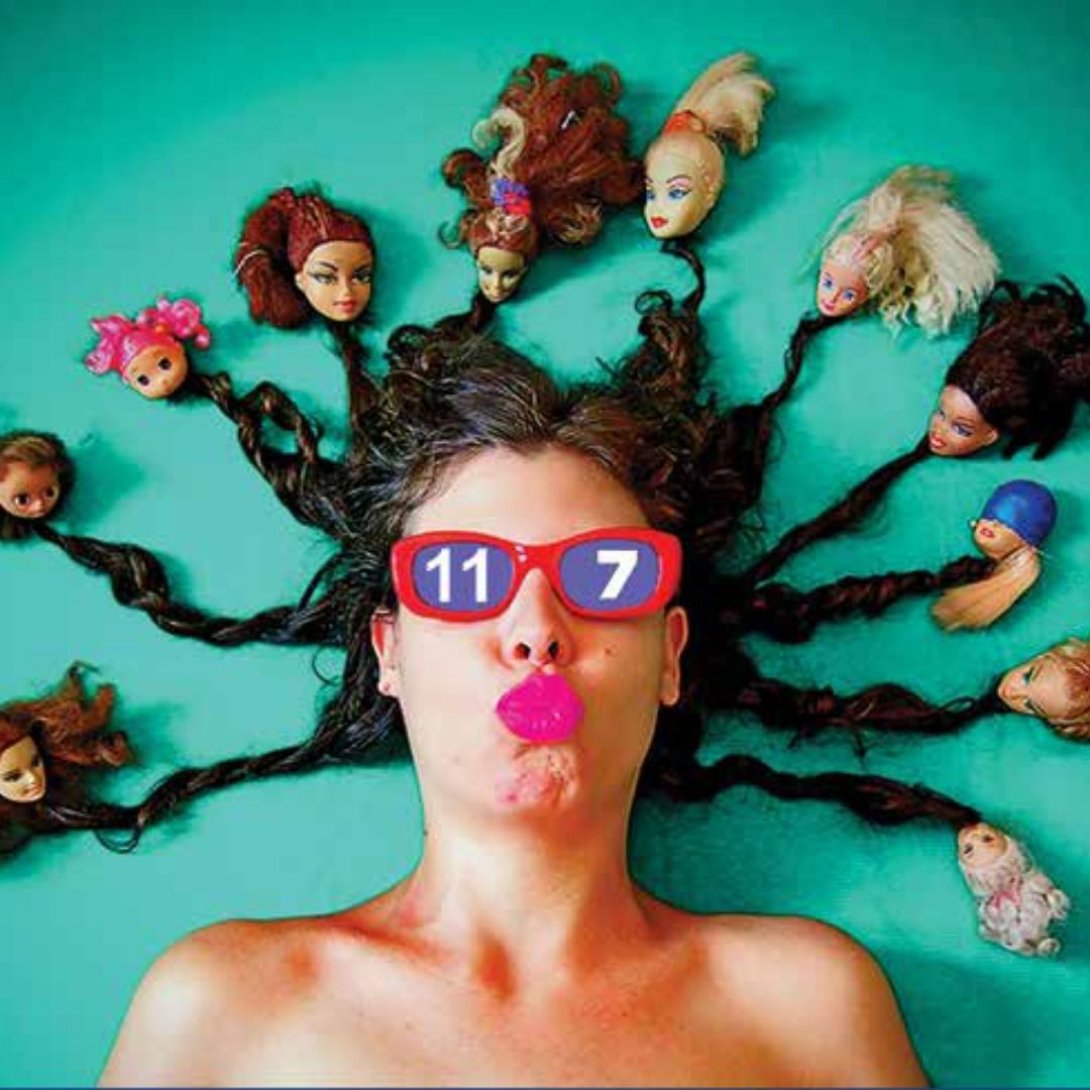 Cartel Medusa 7/11 (2021), de Luis Trápaga. Fotomontaje de mujer con gafas rojas que llevan la fecha 11-7, rodeada de cabezas de muñecas como serpientes.