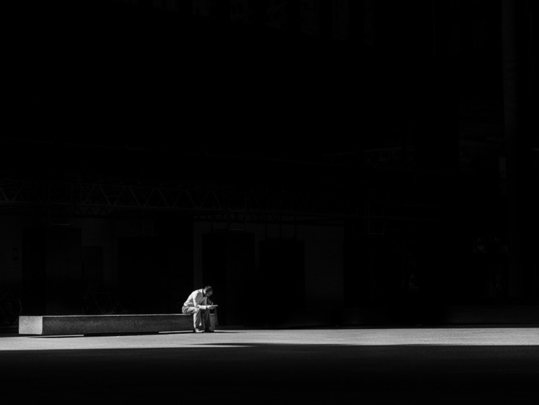 Hombre sentado solo en un banco en la oscuridad en representación de la soledad moral.