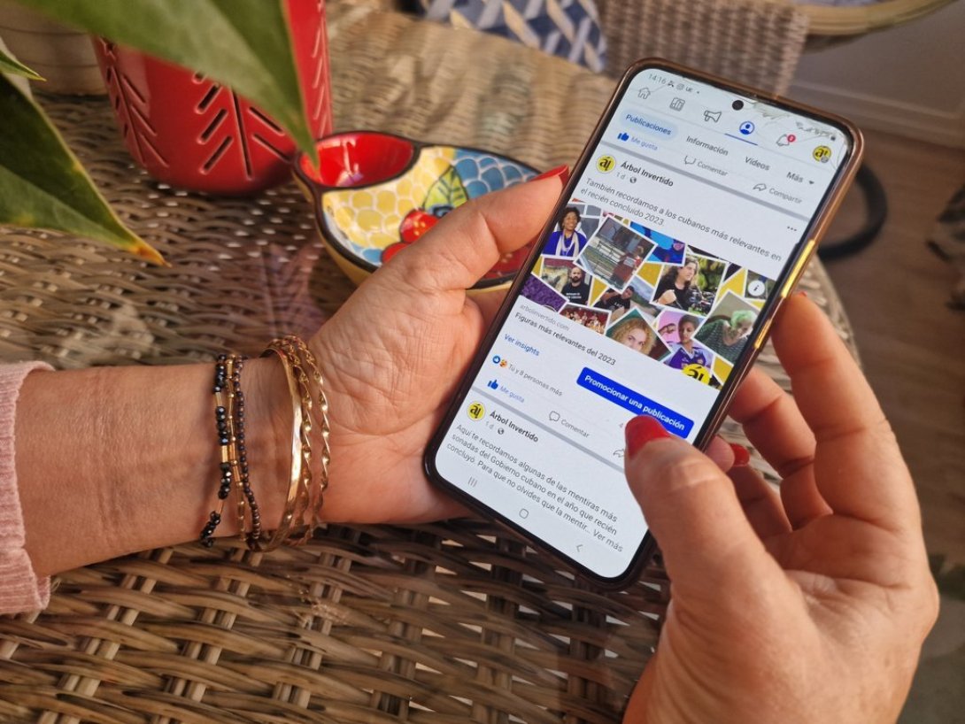 Manos de mujer con teléfono móvil viendo página de Facebook de revista Árbol Invertido redes