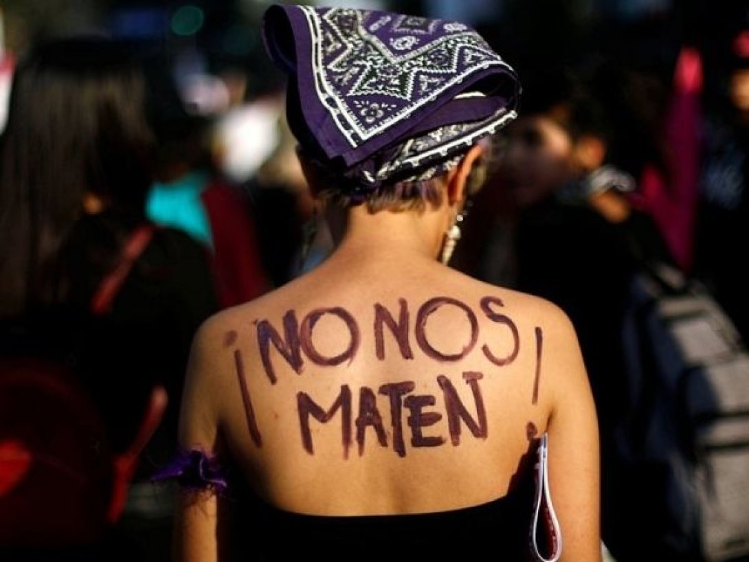 Mujer con pañuelo morado y la frase “¡No nos maten!” pintada en la espalda durante una manifestación feminista.