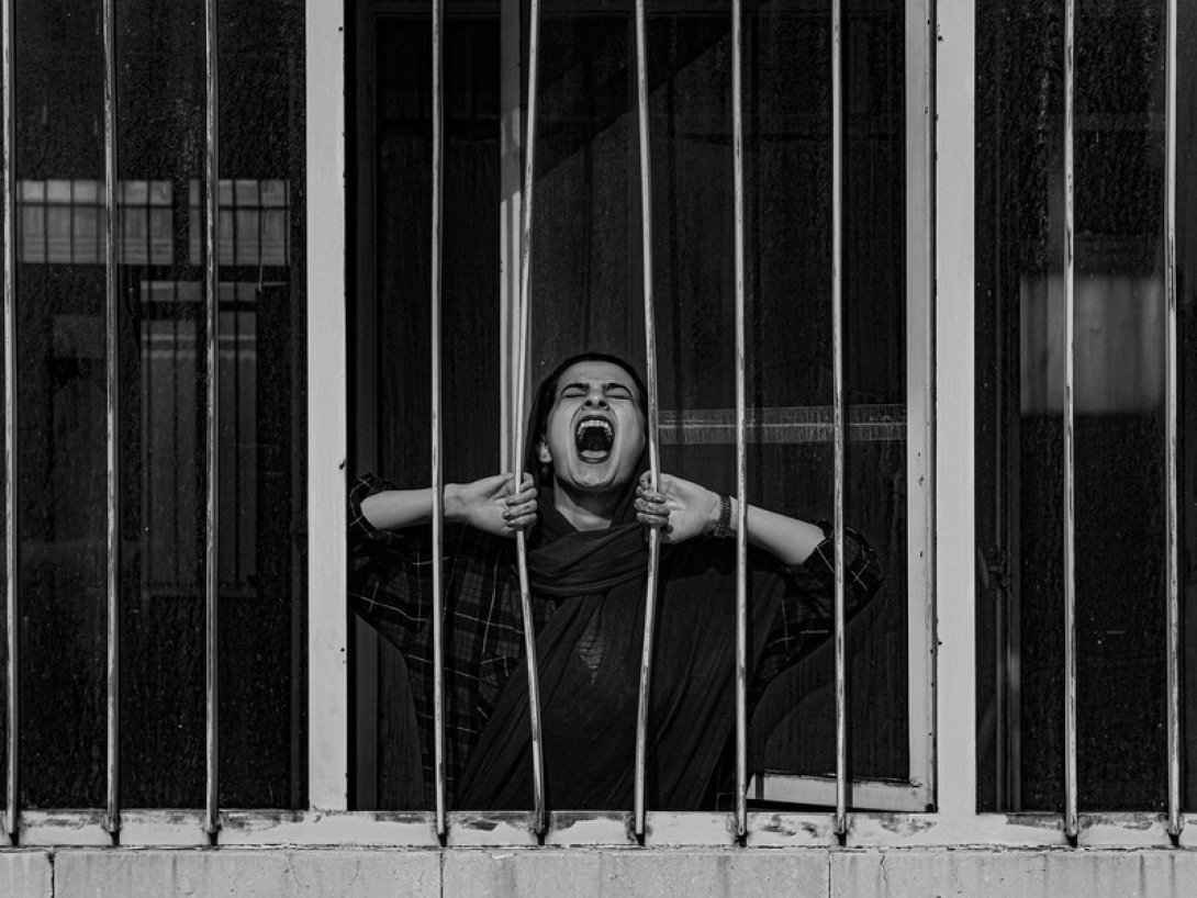 Mujer gritando mientras abre los barrotes de una reja.