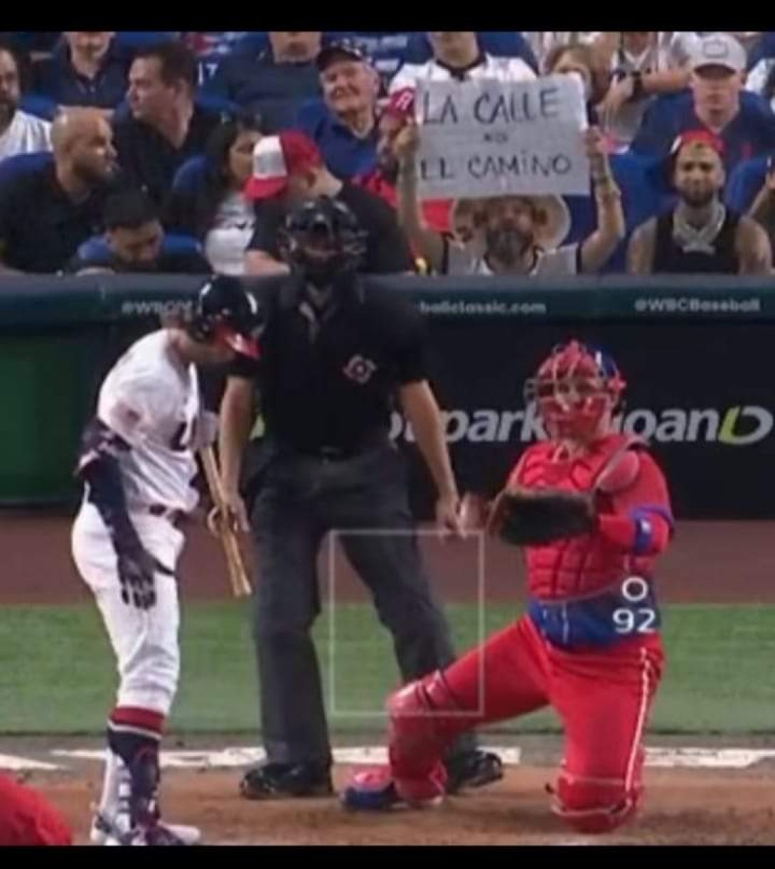 Alexander Otaola muestra un cartel detrás del home plate.