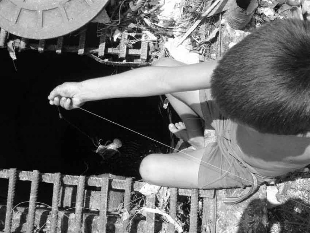 Niño pesca en una alcantarilla