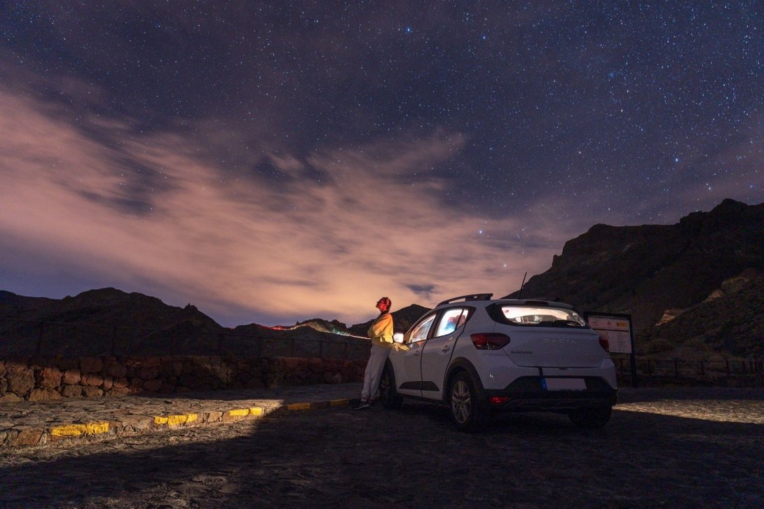 Foto de Atlantic Ambience. Mujer junto a coche y mirando al cielo estrellado.