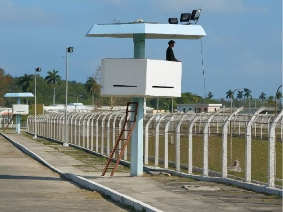 Vista de una prisión en Cuba con torres de vigilancia, un guardia en lo alto y cercas perimetrales con alambre de púas.