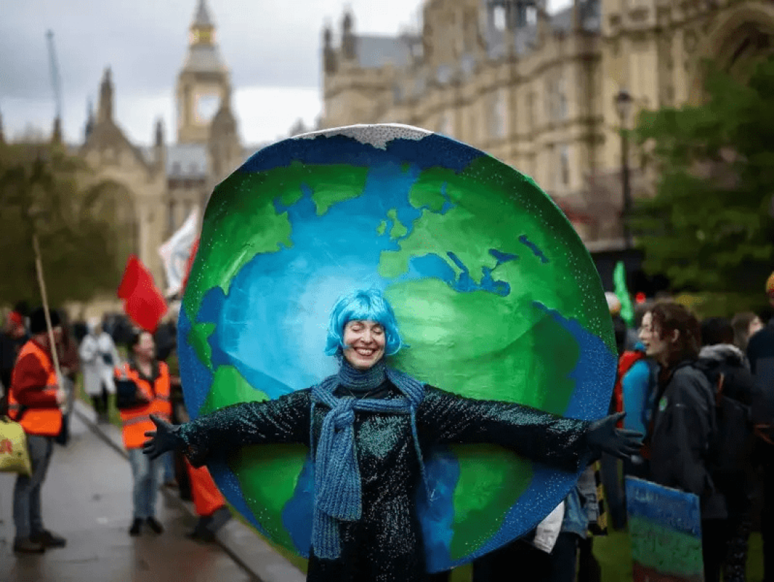 Persona sosteniendo una pelota pintada como el planeta Tierra durante la protesta The Big One en Londres.