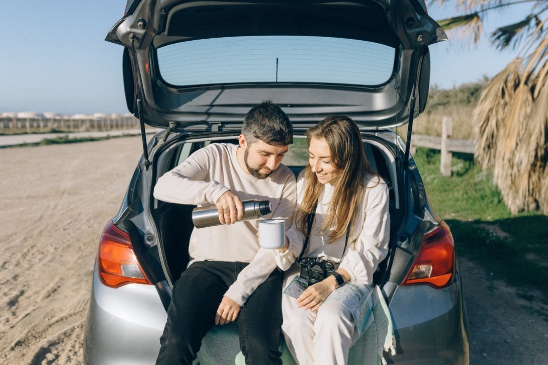Pareja se sirve una bebida mientras descansa junto a su coche durante un viaje por Italia