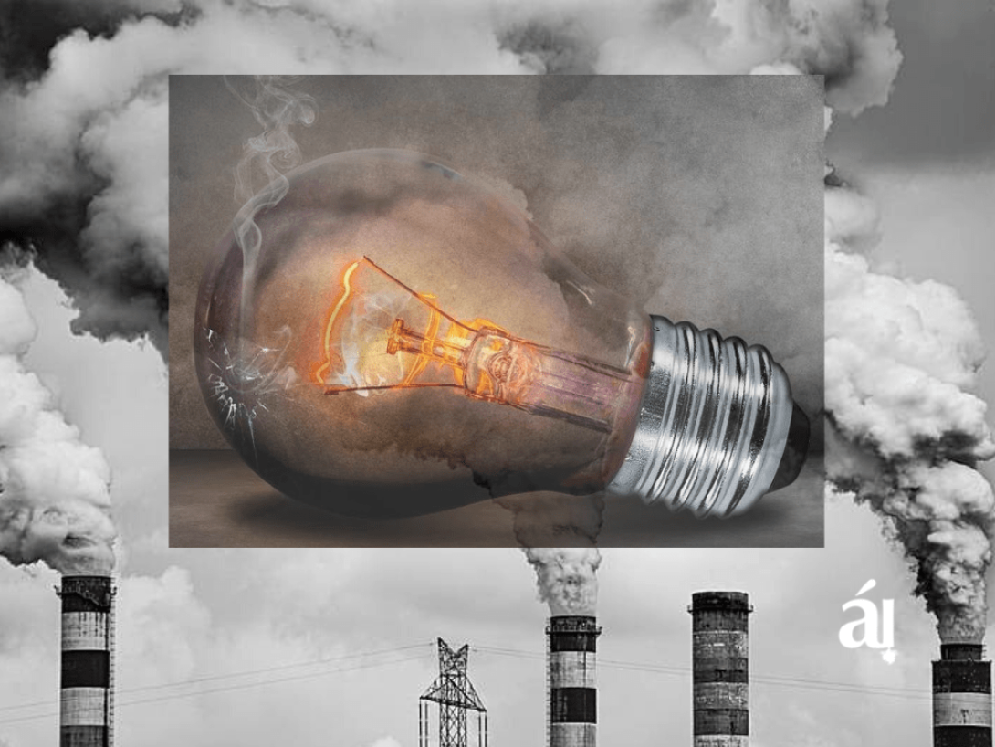 Bombillo roto sobre el humo que provoca la industria de generación de electricidad con combustibles fósiles.