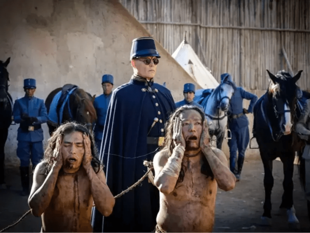 Dos personas arrodilladas y amarradas se llevan las manos a la cabeza en señal de dolor o desconcierto. De pie, otros hombre vestidos de uniforme y con caballos los escoltan.