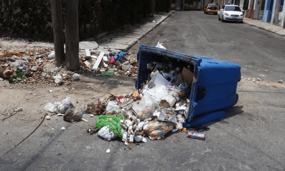 Contenedor de basura volcado en la calle vertiendo la basura alrededor.