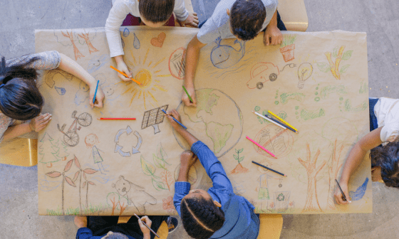 Niños pintando en una mesa dibujos que reflejan el cuidado del medio ambiente.