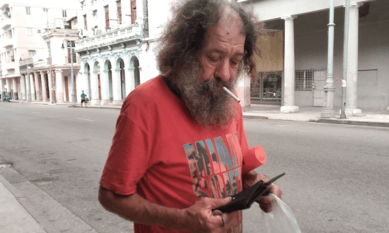 Persona fuma un cigarro en las calles de La Habana mientras mira un celular...