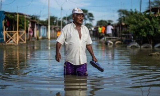 Persona camina por una calle con agua hasta la cintura a causa de una inundación.