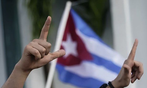 Un manifestante muestra la L de libertad con sus dedos frente a una bandera cubana. Foto: AP