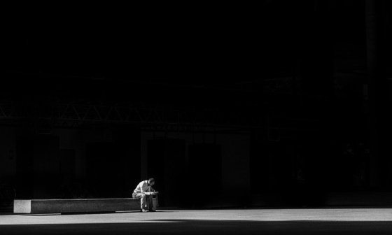 Hombre sentado solo en un banco en la oscuridad en representación de la soledad moral.