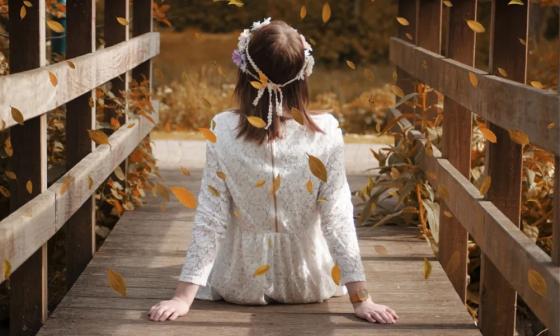 Niña sentada en puente de madera y entre hojas secas cayendo.