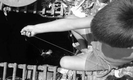 Niño pesca en una alcantarilla